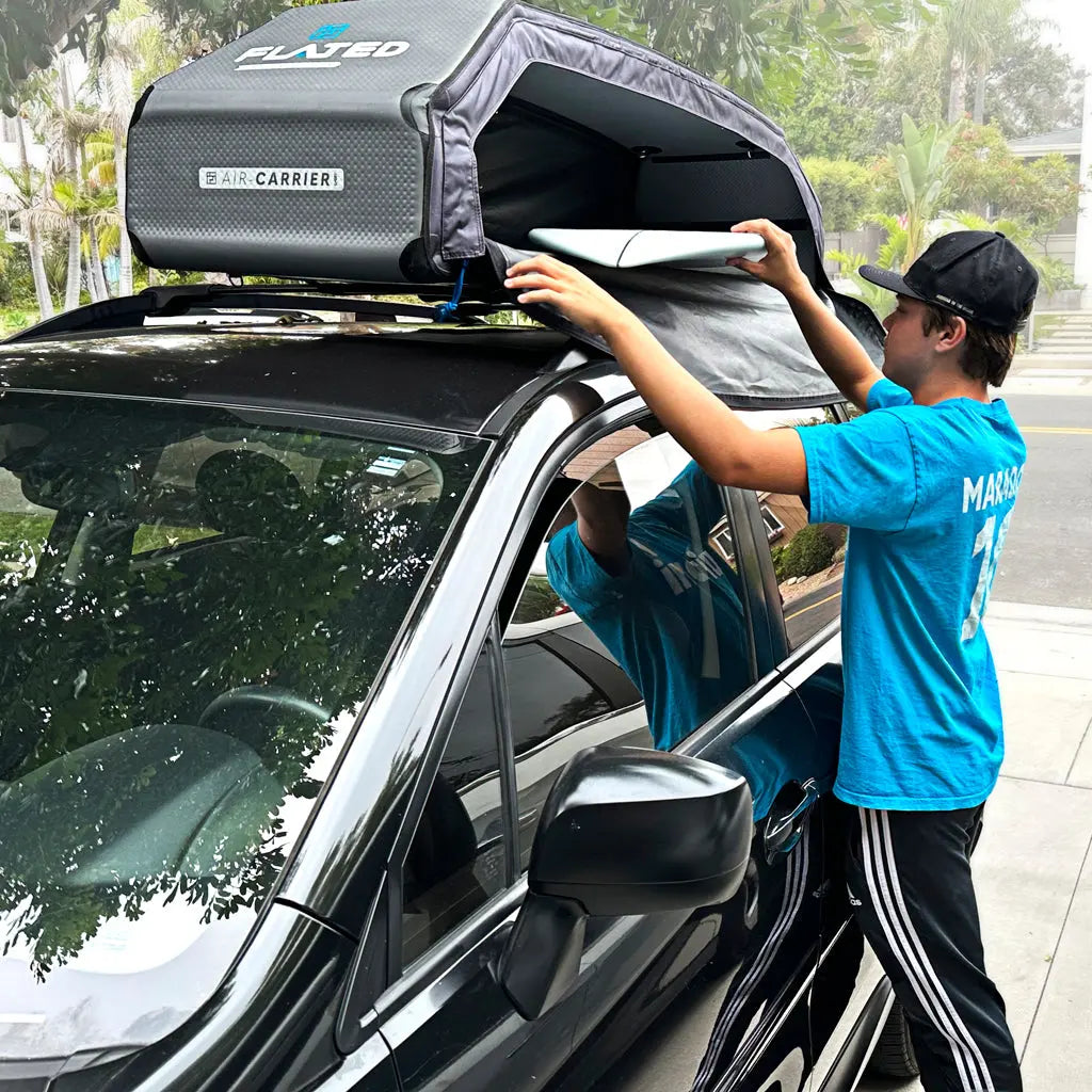 Young Boy loading his surfboard into the Flated Air-Carrier on a Subaru